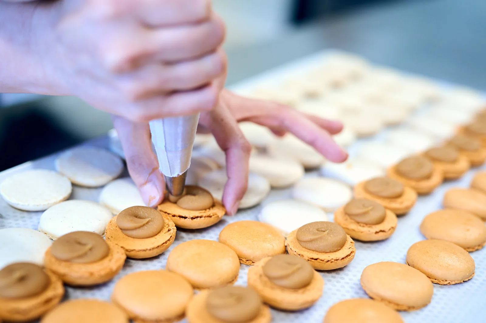 Mains au travail garnissant des macarons, atelier Art & Gourmandise